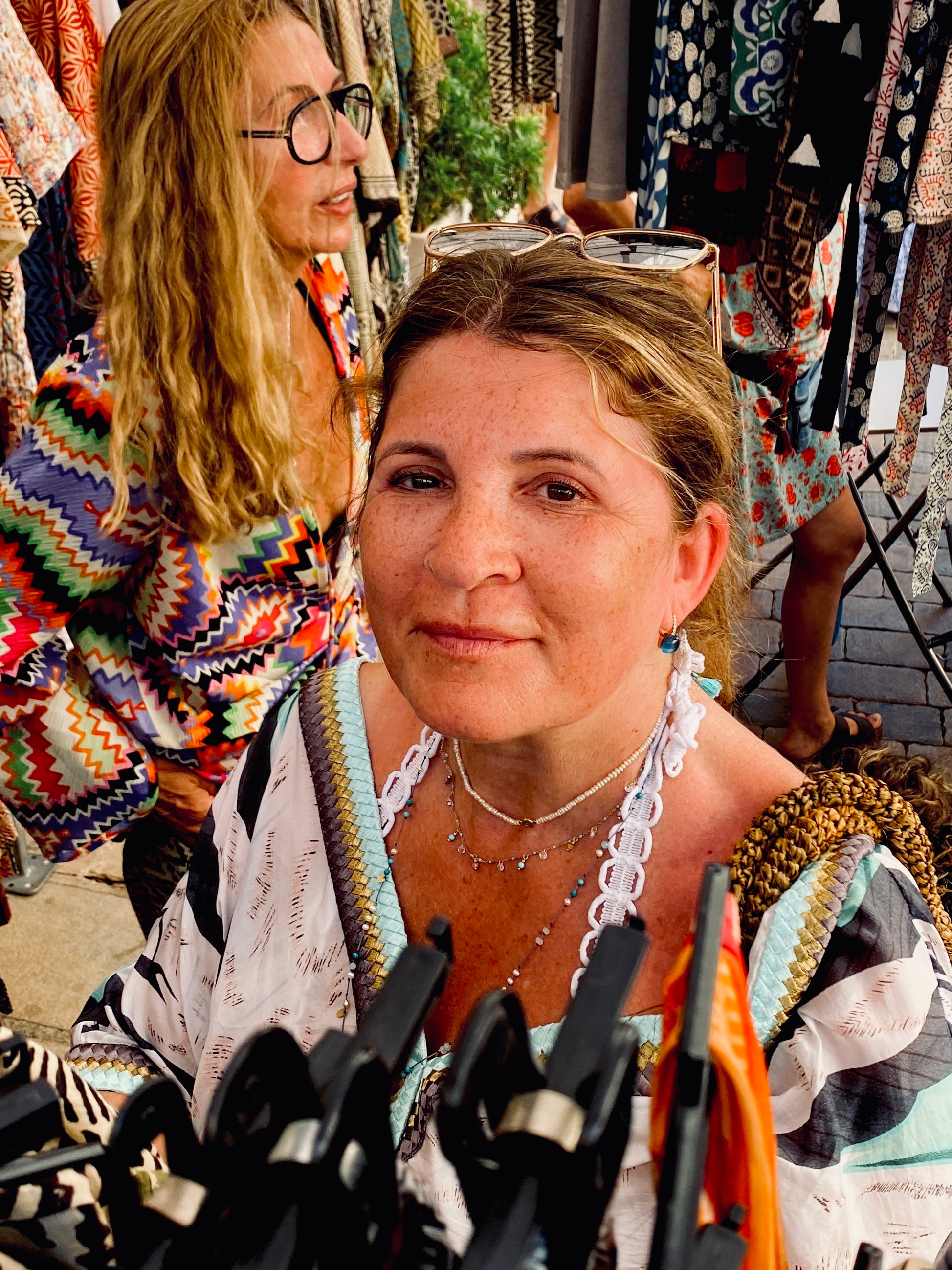 Barbara mit Sonnenbrille im Haar und Perlenkette an einem sommerlichen Boho-Marktstand – Merchant & Friends Friend