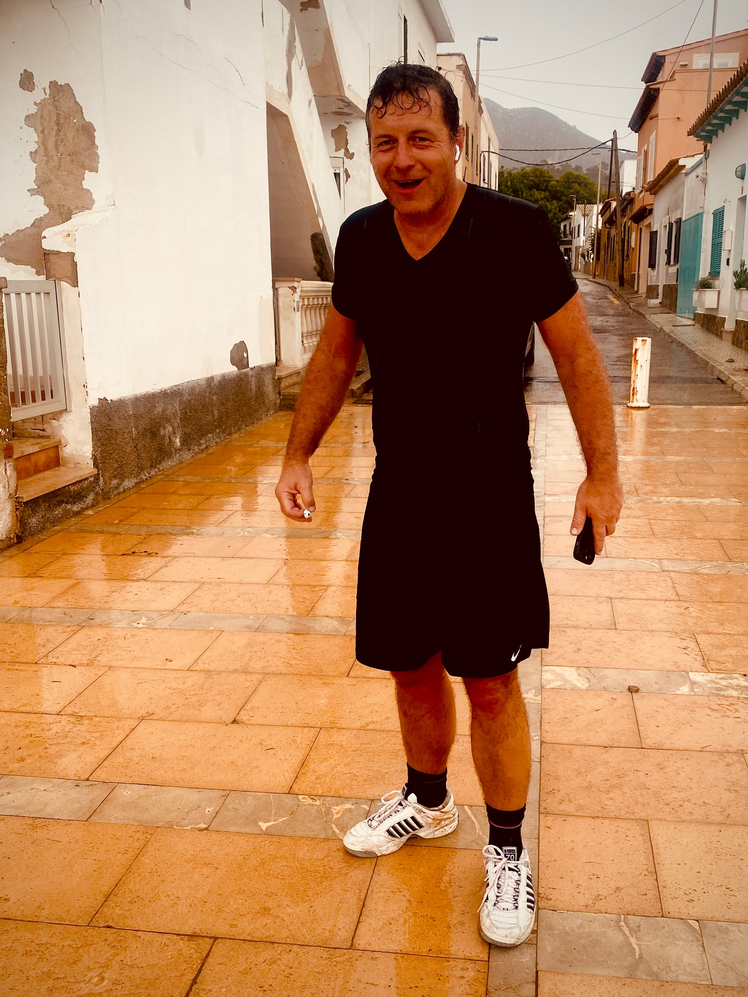 Bernhard in schwarzer Sportkleidung beim Lauftraining in einer mediterranen Gasse nach dem Regen – Merchant & Friends Friend