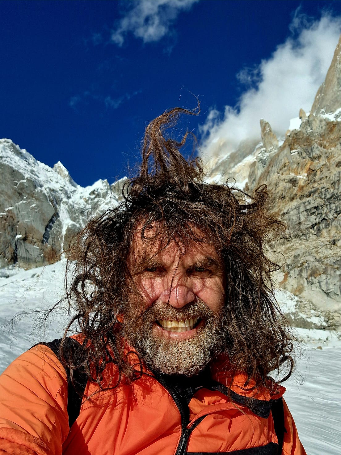 Thomas Huber mit windzerzaustem Haar vor schneebedeckten Gipfeln im Hochgebirge – Merchant & Friends Friend